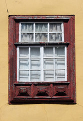 old red painted window frame with white borers on small panes of glass internal white shutters and yellow cracked wall