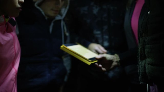 Group hiking in the woods at night using computer tablet for navigation.