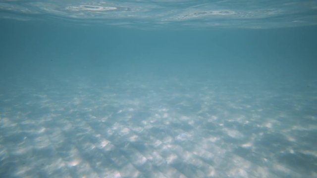 An underwater moving shot of the ocean floor showing blue waters and a white sand ocean floor.