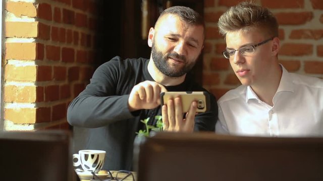 Father showing something on smartphone to his son while sitting in the cafe
