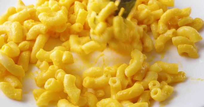 Close video of macaroni and cheese on a white plate being quickly mixed with a fork.