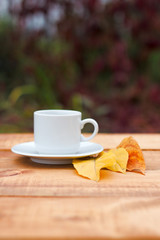 Cup of coffee on old table in autumn with tree maple of colorful leaves in the garden with copy space. Seasonal fall and beautiful relax concept