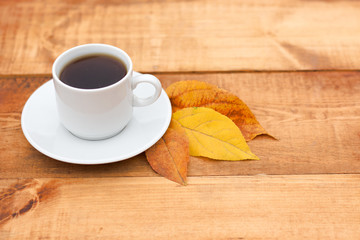 A cup of coffee on wooden table with fallen leaves