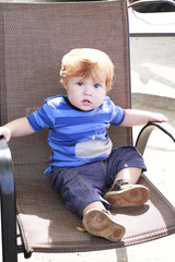 Ginger toddler with blue eyes sitting on chair in outdoor caffe
