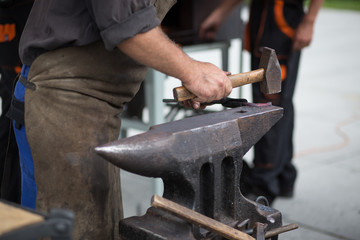 The blacksmith manually forging the molten metal on the anvil in smithy with spark fireworks