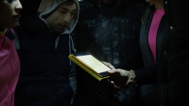 Group hiking in the woods at night using computer tablet for navigation.