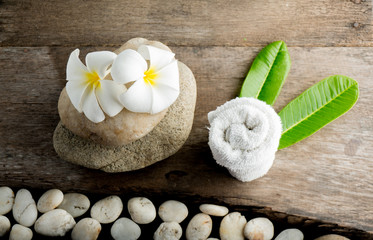 Obraz na płótnie Canvas White flower and leafs with big and tiny stone and towel on wood table for health spa advertisement and presentation