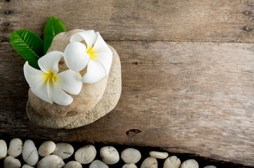 White flower and leafs with big and tiny stone and towel on wood table for health spa advertisement and presentation