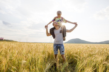 Fototapeta na wymiar young father with his little son walking in the wheat field at sunset in a warm summer day