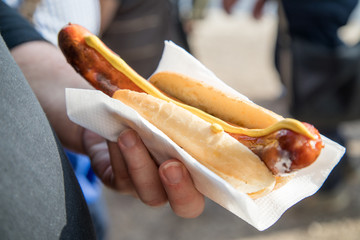 Männliche Hand mit Krakauer und Senf im Brötchen