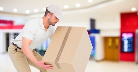 Delivery man picking up box against blurry shopping centre