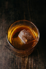 Old fashioned cocktail with a cube of ice on rustic background