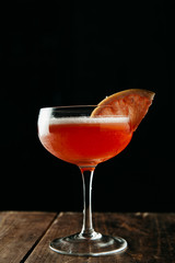 Pink cocktail garnished with a slice of blood orange on dark background