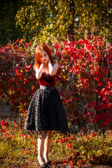 Charming redhead lady in vintage skirt and red velvet top. Stylish woman in autumn garden, pretty girl in retro doll style 