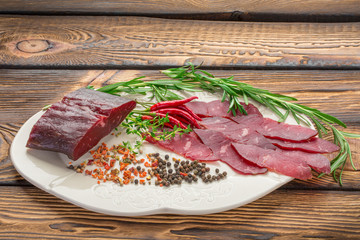 delicious sliced pieces jerky lie on a wooden background, around the chilli pepper, herbs, spices