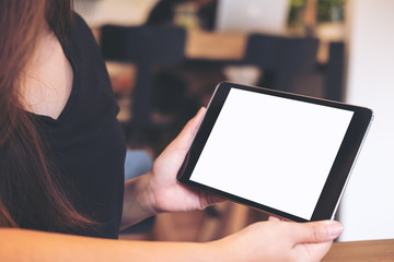 Mockup image of a beautiful Asian business woman holding and looking at black tablet pc with blank white screen in modern cafe