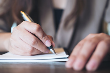 Closeup image of business woman writing on blank notebook on wooden table