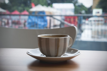 Closeup image of hot coffee cup on wooden table in cafe with outdoor background