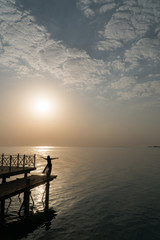 A girl in a swimsuit and a cloak is standing on the pier and meets the dawn