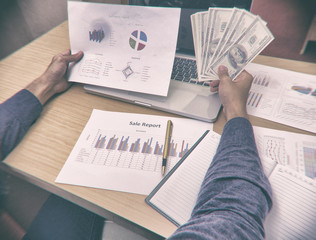 Naklejka premium The blurry design backgroud of paper investment chart and money,they were holding by business worker hand,dramatic tone,abstract art design,vintage art style,grainy film and classic old film style,