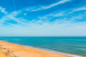 View of the sand shore of ocean and sky with contrails in sunny hot day
