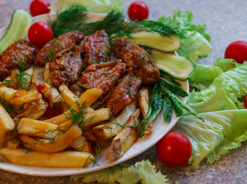 Chicken ribs in honey sauce with French fries and vegetables.