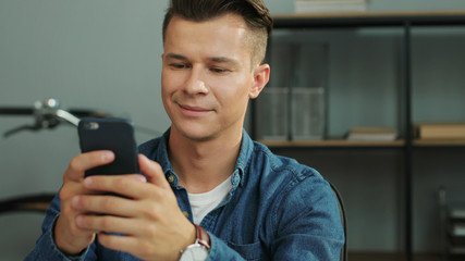 Young attractive business man typing in the smart phone while sitting in the office. Portrait shot.