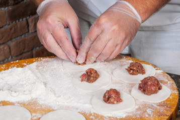 chef hands in process of making home-made dumplings, ravioli or pelmeni