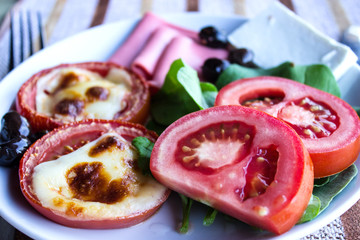 Fresh tomatoes, baked with cheese, ham, olives and lettuce. Breakfast. Close-up. Selective focus.