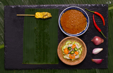 Pork satay skewer with peanut sauce decorated with cucumber sauce, onion, chili on banana leaf.