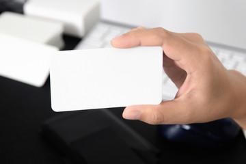Blank business card mock up in hand on blurred office desk background use us contact information design templete