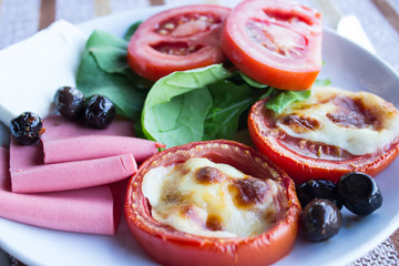 Fresh tomatoes, baked with cheese, ham, olives and lettuce. Breakfast. Close-up. Selective focus.