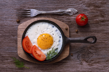 Fried eggs in a cast-iron frying pan with tomatoes and black pepper.
