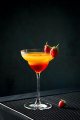 Red and yellow classic sex on the beach alcohol cocktail with fruit juice and strawberries and ice cubes with strawberries on black background in dark bar table
