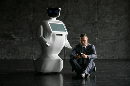 businessman uses a smartphone while sitting on the floor next to a robot. Modern Robotic Technologies. Humanoid autonomous robot. loft office