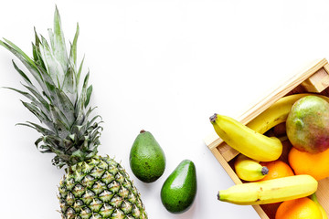 Sell friuts on the market. Bananas, oranges, mango in box and pineapple on white top view copyspace