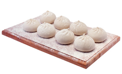 Fashioned khinkali lie on a wooden board sprinkled with flour.