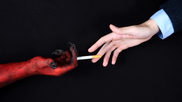 Demon hand gives a cigarette to the man. Top view.