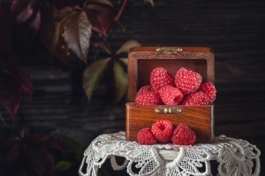Beautiful ripe raspberries in the autumn in a wooden box on the white table cloth of lace. Close-up. Copy space.