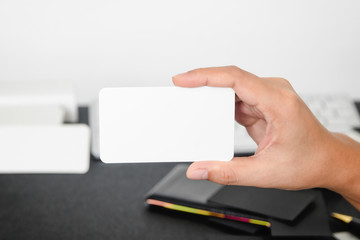 Obraz premium Blank business card mock up in hand on blurre office desk background use us contact information design templete