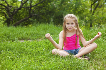 Naklejka na ściany i meble A beautiful young girl sits on a green grass in a yoga pose