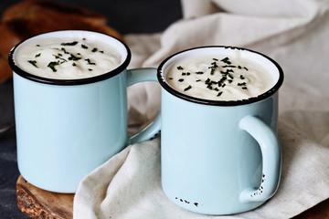 Hot potato soup with dried chives served in enamel cups with sliced, toasted bread. Extreme shallow depth of field with selective focus on cup in foreground.