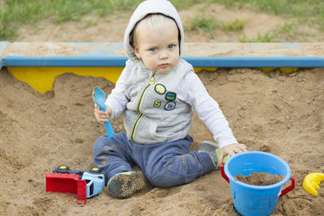 Adorable one year toddler playing with toys and sand in sandbox