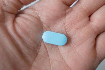 Eine männliche Hand hält eine blaue Pille