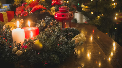 Advent wreatch on table with burning candles next to decorated Christmas tree