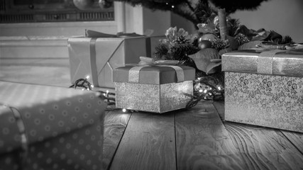 Black and white image of gifts in boxes on wooden floor under Christmas tree