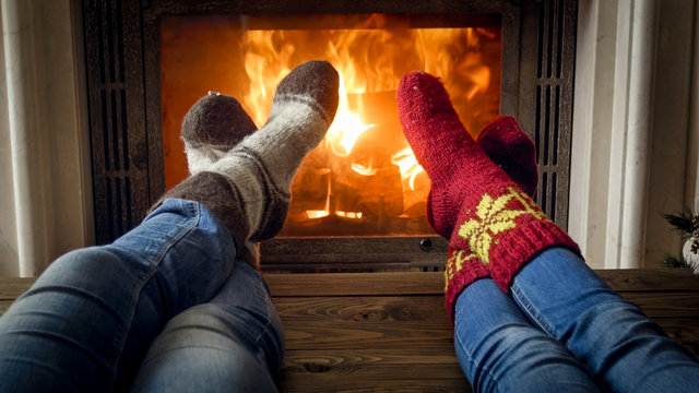 Young Couple In Warm Knitted Socks Relaxing In Chalet At Fireplace