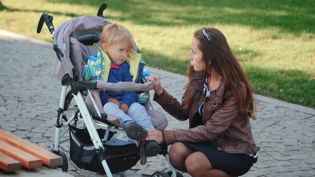 Sad caucasian child, kid toddler , little baby boy talking with mother while sitting in stroller . Childhood dreams and memories. Autumn park. Slow motion