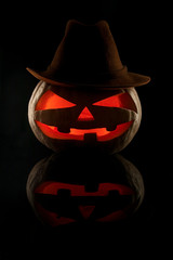 The concept of Halloween. Evil scary pumpkin cowboy in a hat in the dark with a reflection. Jack Lantern in the darkness