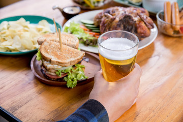 The beer glass is put on the table with the man's hand. There are sandwich and many food.